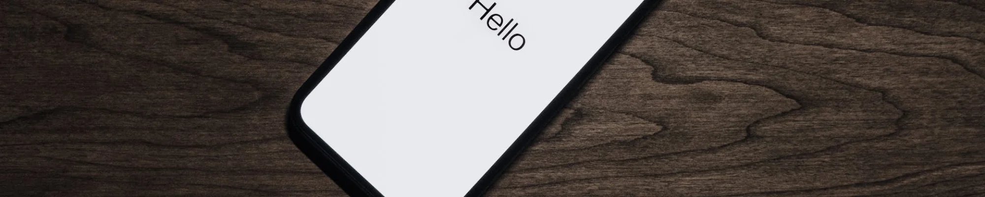 Mobile phone on a wood surface. The screen reads "hello"